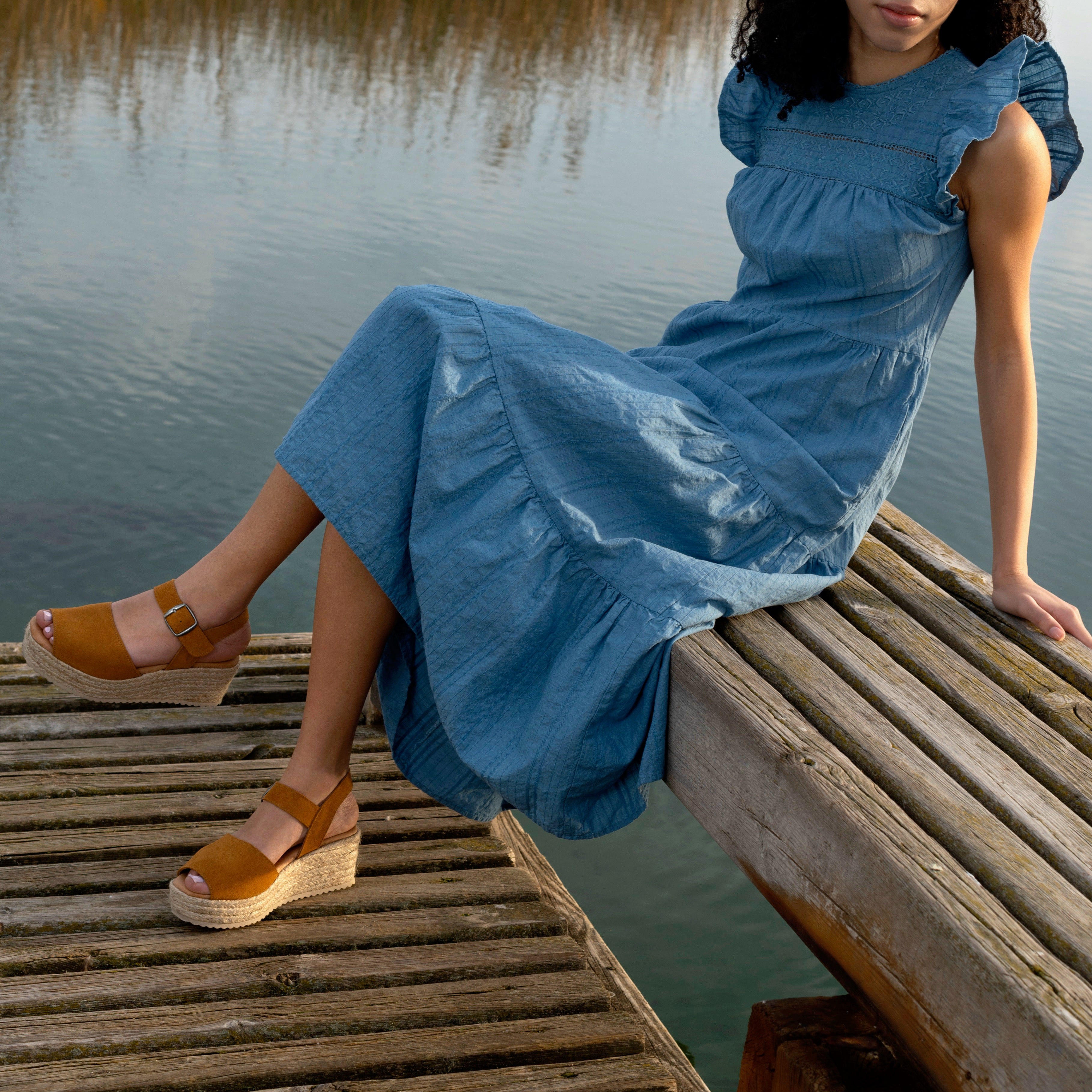 woman sitting by a like wearing a blue dress and platform sandals in whiskey color