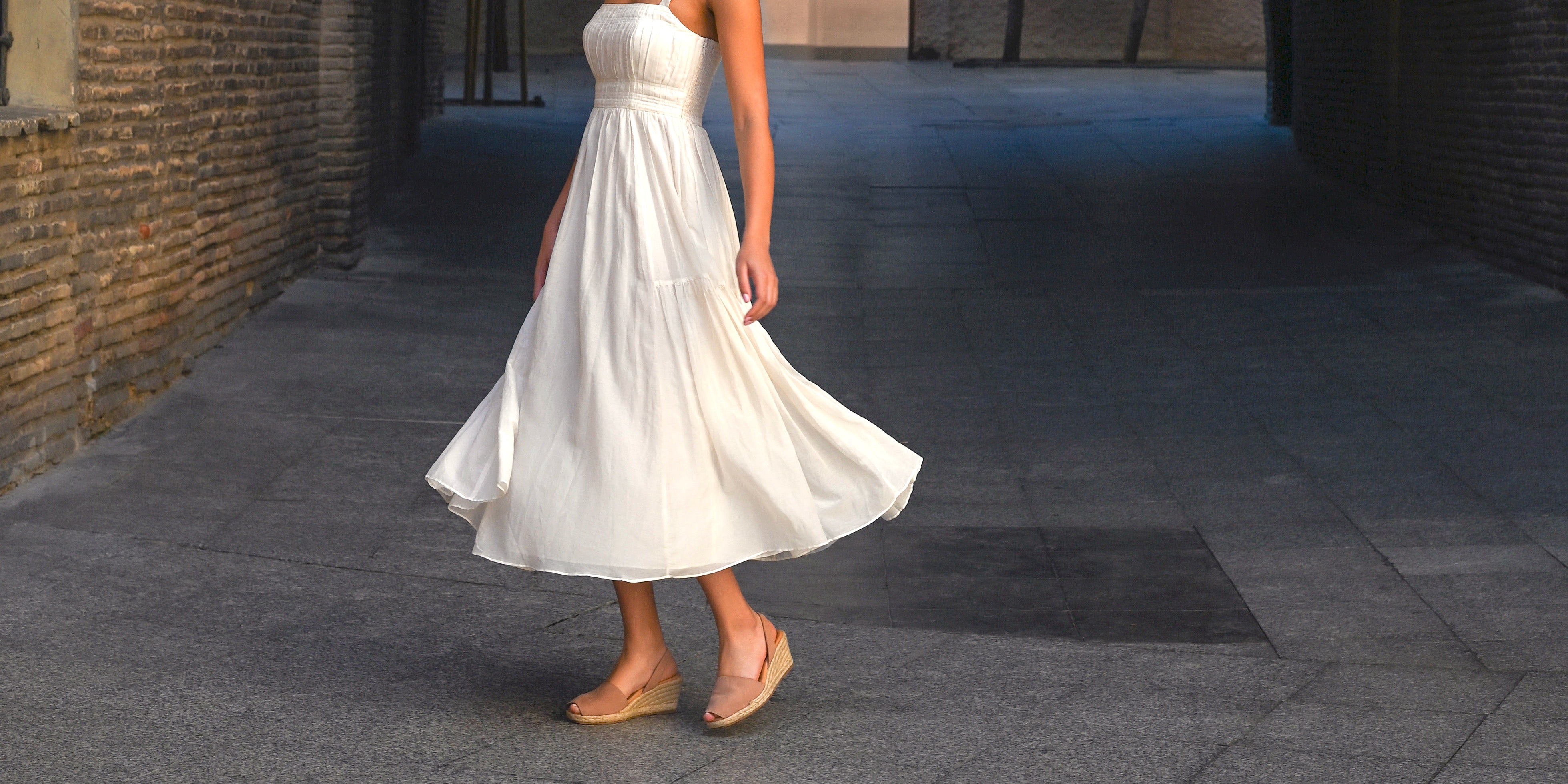 Woman twirling while wearing white dress and tan nubuck wedge sandals